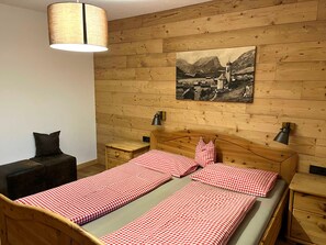 Una habitación con paneles de madera, una cama, dos mesitas de noche, una lámpara, una silla y un cuadro colgado en la pared.