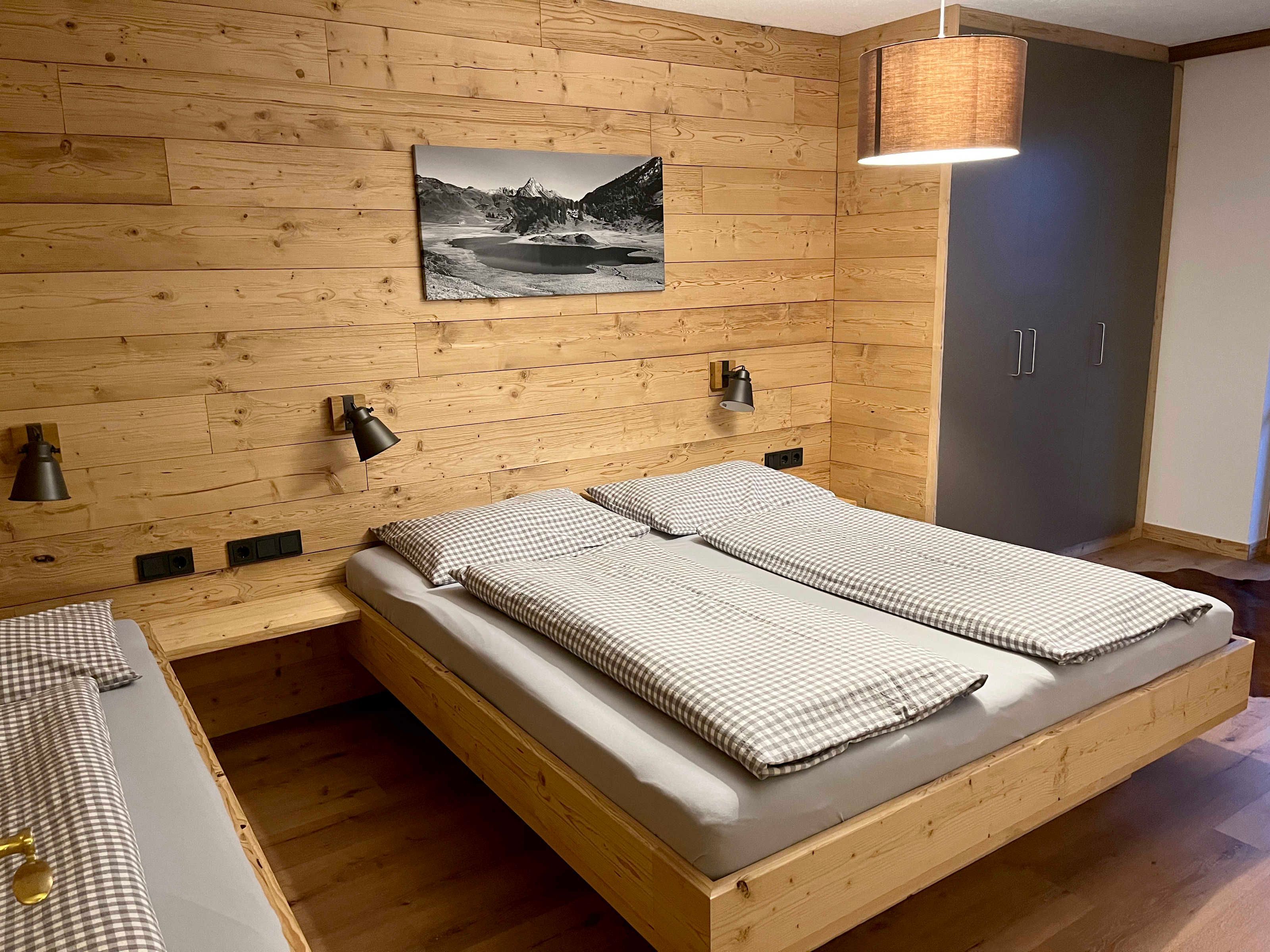 A wooden-paneled bedroom with a bed, bedside lamps, and a wall-mounted picture.