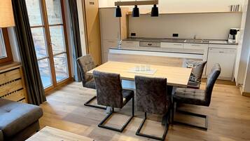 A modern kitchen with a dining area, wooden flooring, and a large window with curtains.