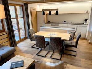 Una cocina moderna con comedor, piso de madera y un amplio ventanal con cortinas.
