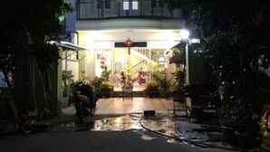 A two-story building with a central entrance, surrounded by potted plants and a motorcycle.