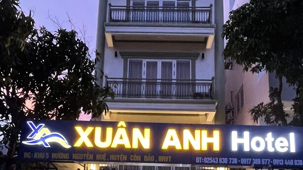 The exterior of Xuan Anh Hotel with a signboard displaying the hotel's name and contact information.