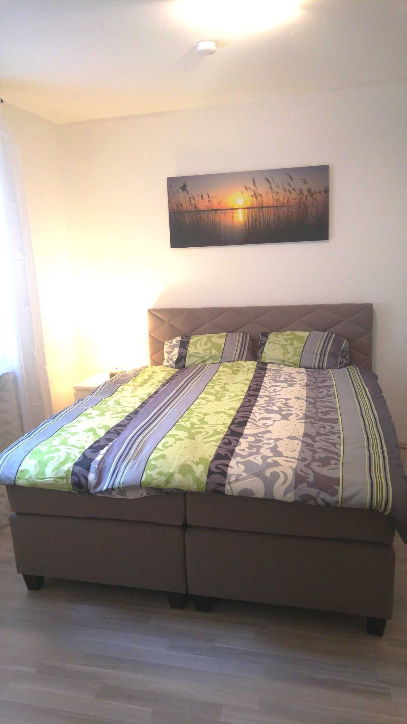 Ein Schlafzimmer mit einem Bett, einem Bild an der Wand und einem Fenster mit Vorhängen.
