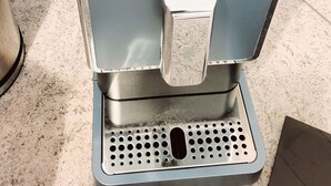 En kaffemaskin med en svart överdel och en silverfärgad bas, fylld med kaffebönor.