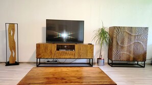 Ett modernt vardagsrum med en möbel i trä för underhållningssystemet, en platt-TV, ett soffbord i trä och dekorativa föremål, inklusive en växt och en väggpanel med intressant struktur.