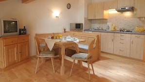 Una cocina acogedora con armarios de madera, una mesa de comedor con sillas y un televisor sobre un mueble.