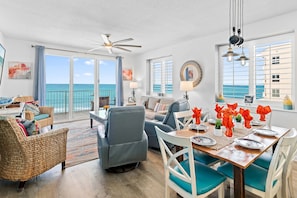 A spacious living area with a balcony overlooking the sea, a dining table set with chairs, and a ceiling fan.