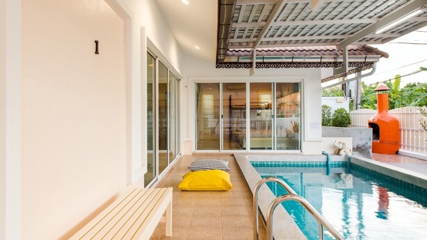 Ein Poolbereich mit einer Sitzbank, einer Glastür zu einem Raum und einer überdachten Terrasse.