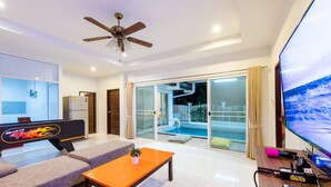 Ein modernes Wohnzimmer mit Blick auf einen Pool, einem Deckenventilator und einem Flachbildfernseher.