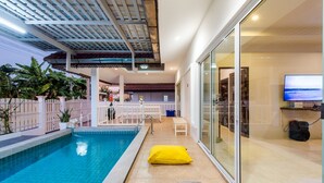 Ein überdachter Swimmingpool mit Glaswand, einer Sitzbank und einem gelben Kissen.