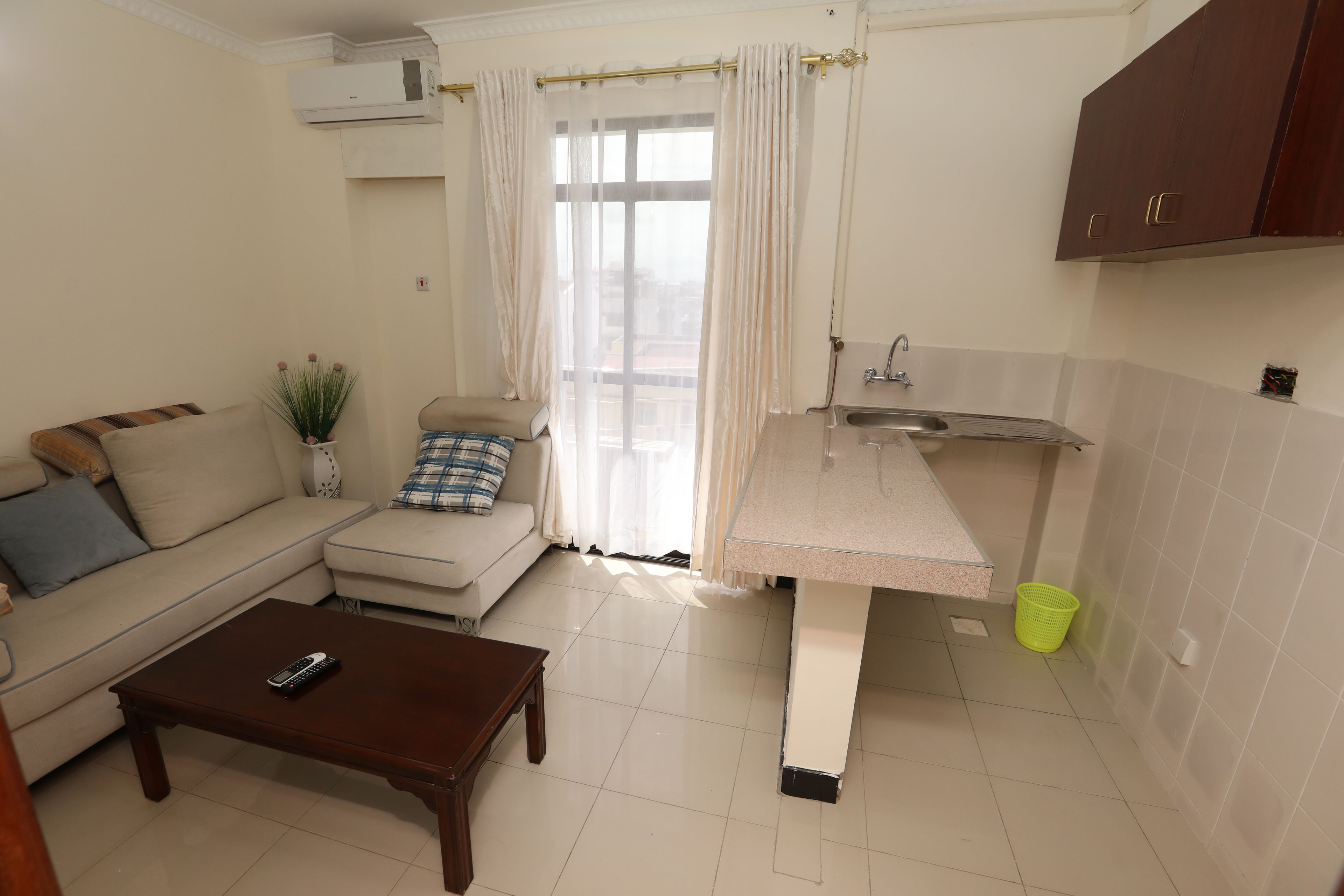 A compact living space with a sofa, a small coffee table, a kitchenette with a sink and countertop, and a window with curtains.