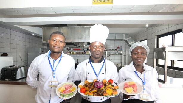 Three individuals in a kitchen holding plates of food. - Sheratton Regency Hotel (Mombasa)