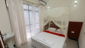 A neatly arranged bedroom with a bed, a bedside table, a sink, and a window with curtains. - Sheratton Regency Hotel (Mombasa)