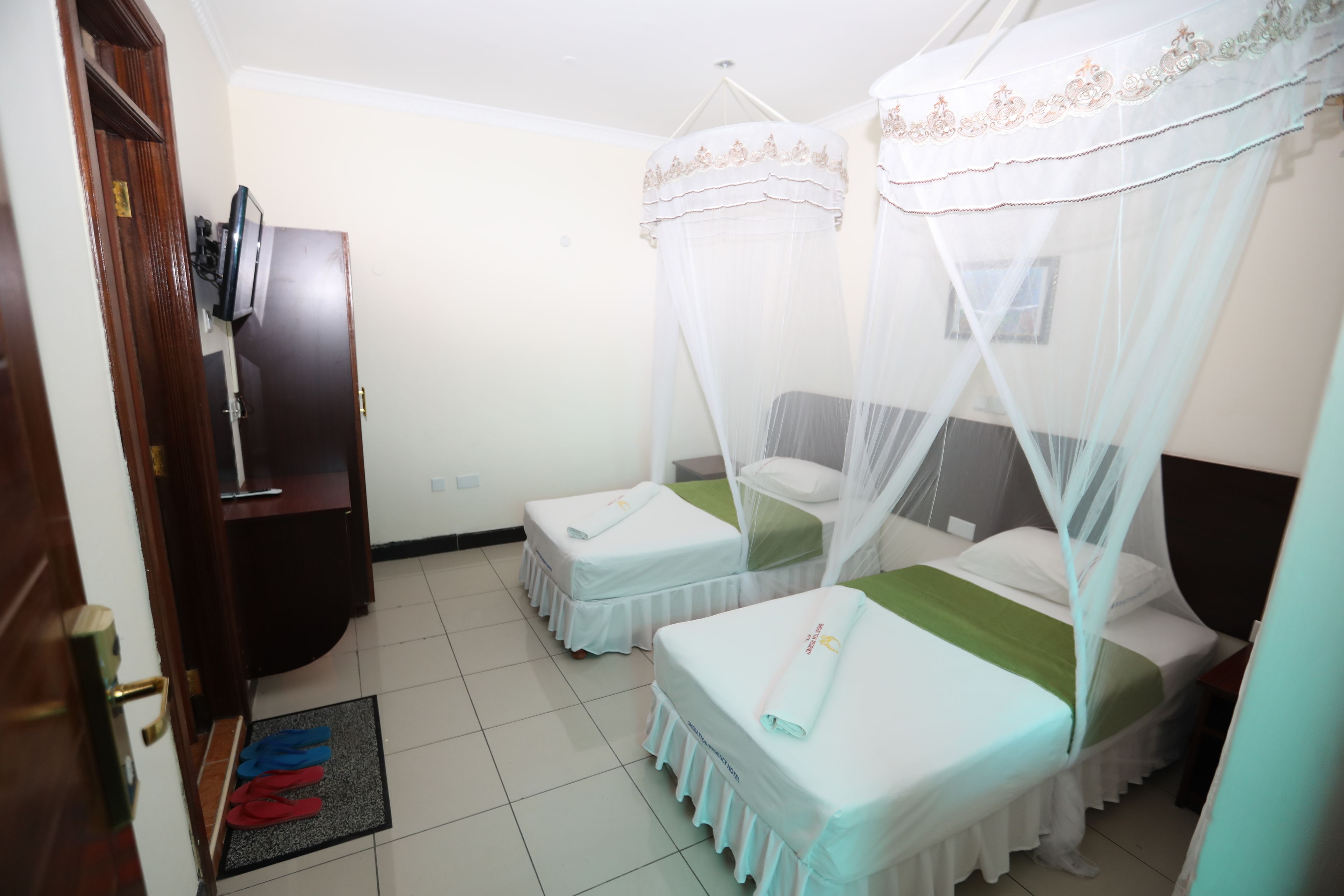 A hotel room with two beds, each with a canopy, a television, and a wooden wardrobe.