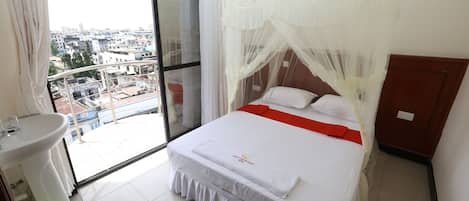 Habitación de hotel con balcón, cama con dosel, lavamanos y una cesta verde.