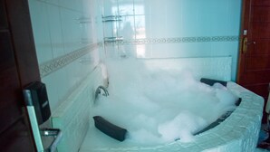 A bathroom with a large bathtub filled with bubbles, a shower area, and a tiled wall with a decorative border. - Sheratton Regency Hotel (Mombasa)