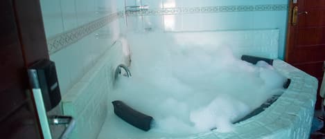 A bathroom with a large bathtub filled with bubbles, a shower area, and a tiled wall with a decorative border.