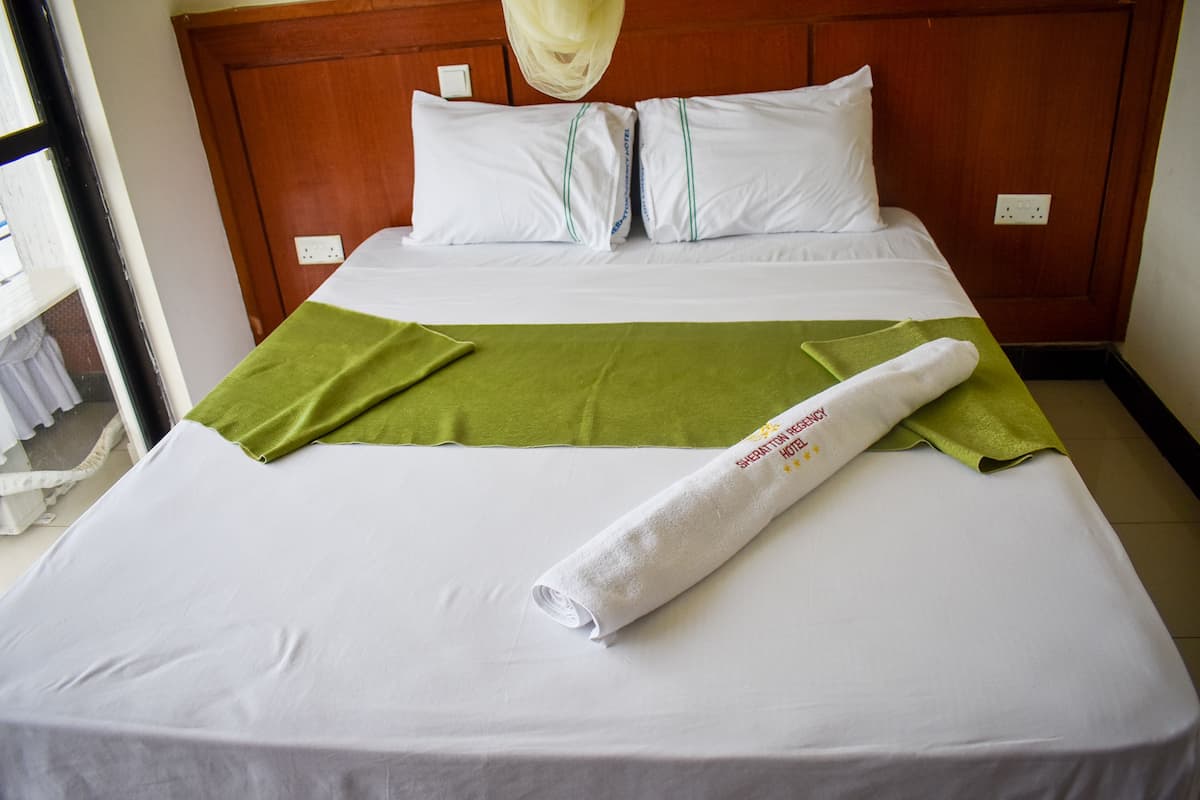 A neatly made bed with white linens, a green towel, and a rolled white towel with text.