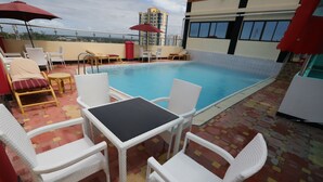 A rooftop pool area with white wicker chairs and a table, red umbrellas, and a view of a cityscape. - Sheratton Regency Hotel (Mombasa)