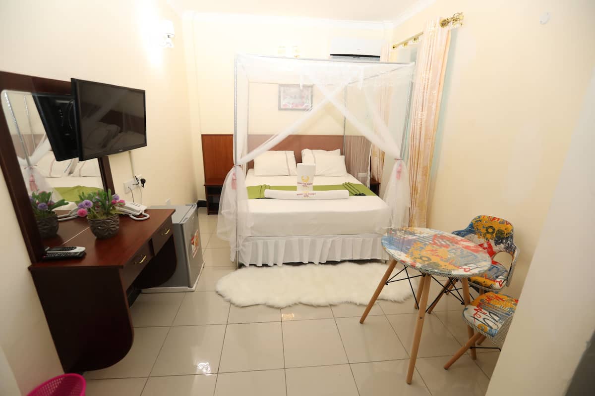 A hotel room with a bed, a desk with a computer, a TV, and a small table with chairs.