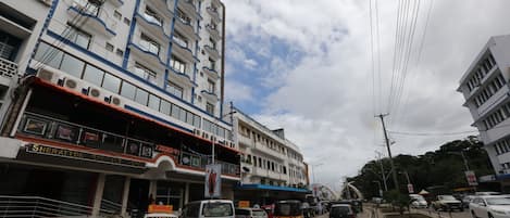 Un hotel a più piani con balconi, un cartello con la scritta Sheraton Regency Hotel e diversi veicoli sulla strada.