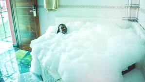 A bathroom with a bathtub filled with foam, a towel hanging on the wall, and a glass door. - Sheratton Regency Hotel (Mombasa)