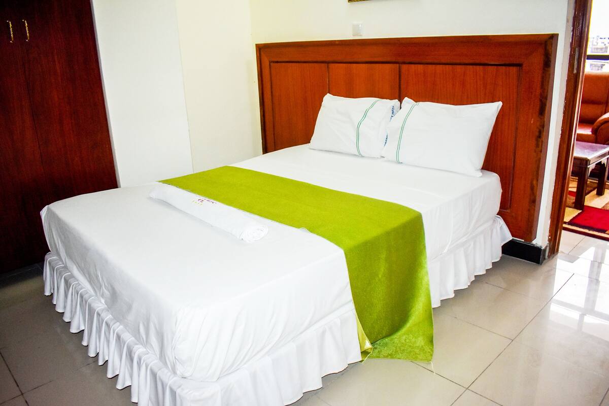 A hotel room with a large bed, a wooden headboard, and a green runner.
