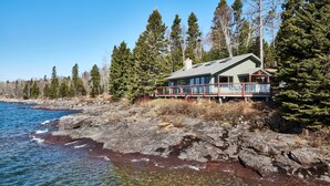 A coastal house with a deck overlooking the water, surrounded by trees. - 'Reflections' Cabin on Lake Superior - Near Lutsen (Schroeder)