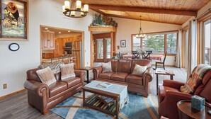 A spacious living room with leather sofas, a coffee table, and a dining area with a view. - 'Reflections' Cabin on Lake Superior - Near Lutsen (Schroeder)
