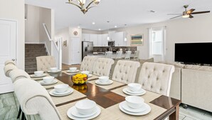 A dining area with a long table set for six, a chandelier, and a ceiling fan.
