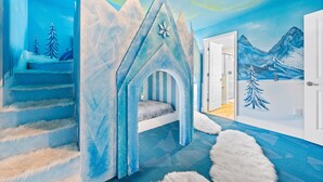 A children's playroom with a snowy mountain mural, a bed, and a staircase.