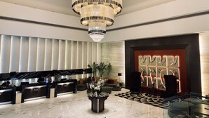 A hotel lobby with a reception desk, a large chandelier, a patterned floor, and a modern wall design. - The Landmark Hotel (Kanpur)
