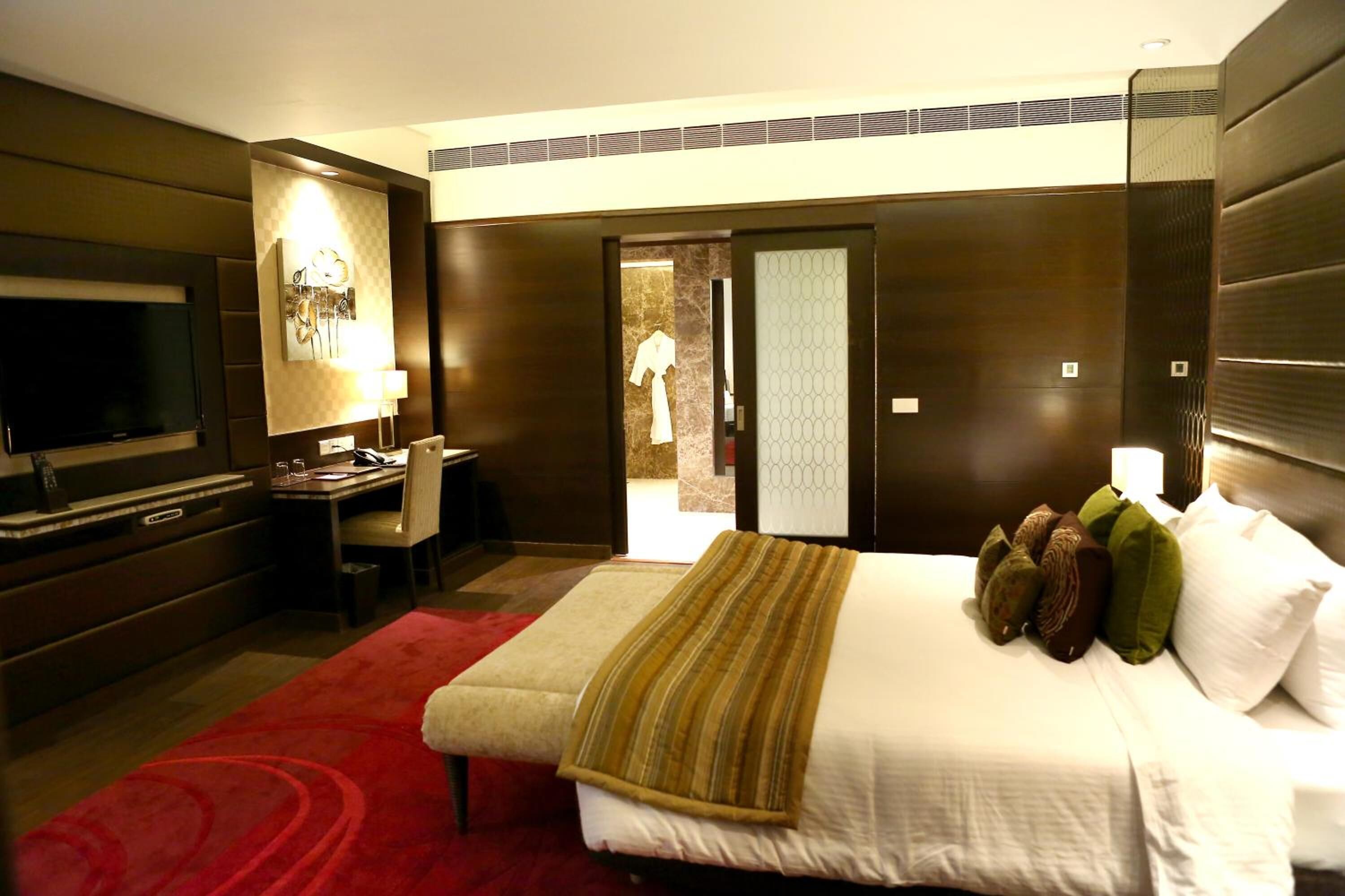A hotel room with a bed, a desk, a TV, and a red carpet.