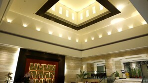 A spacious lobby with a high ceiling, a central skylight, and a reception desk. - The Landmark Hotel (Kanpur)