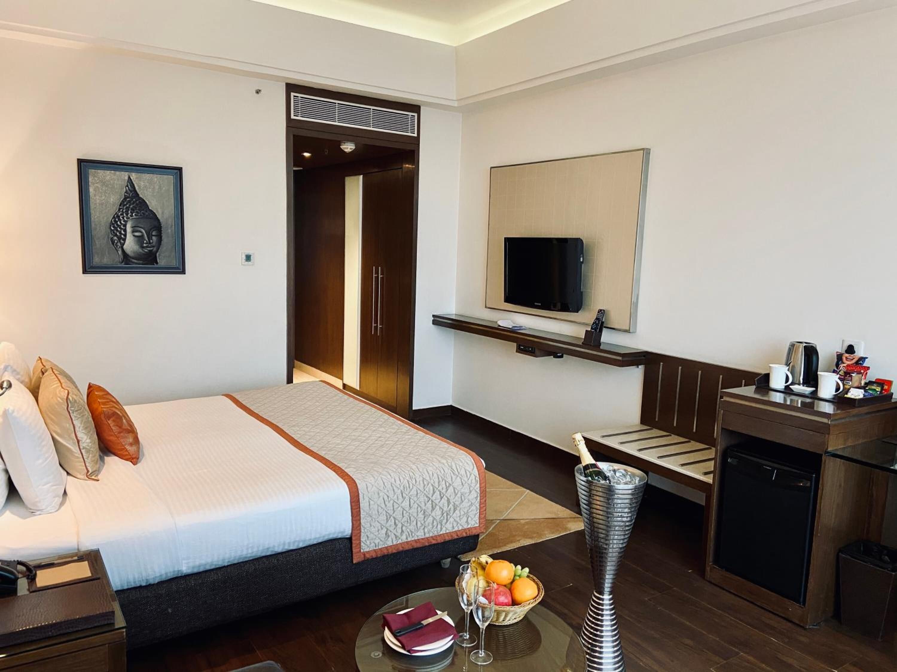 A hotel room with a bed, a TV, a small kitchenette, and a dining area.