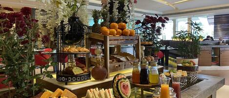 Ein Buffet mit verschiedenen Speisen, darunter Sandwiches, Gebäck und eine Wassermelone mit Herzdesign.