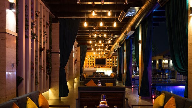 A modern interior with a bar area, seating, and a pool view. - The Landmark Hotel (Kanpur)