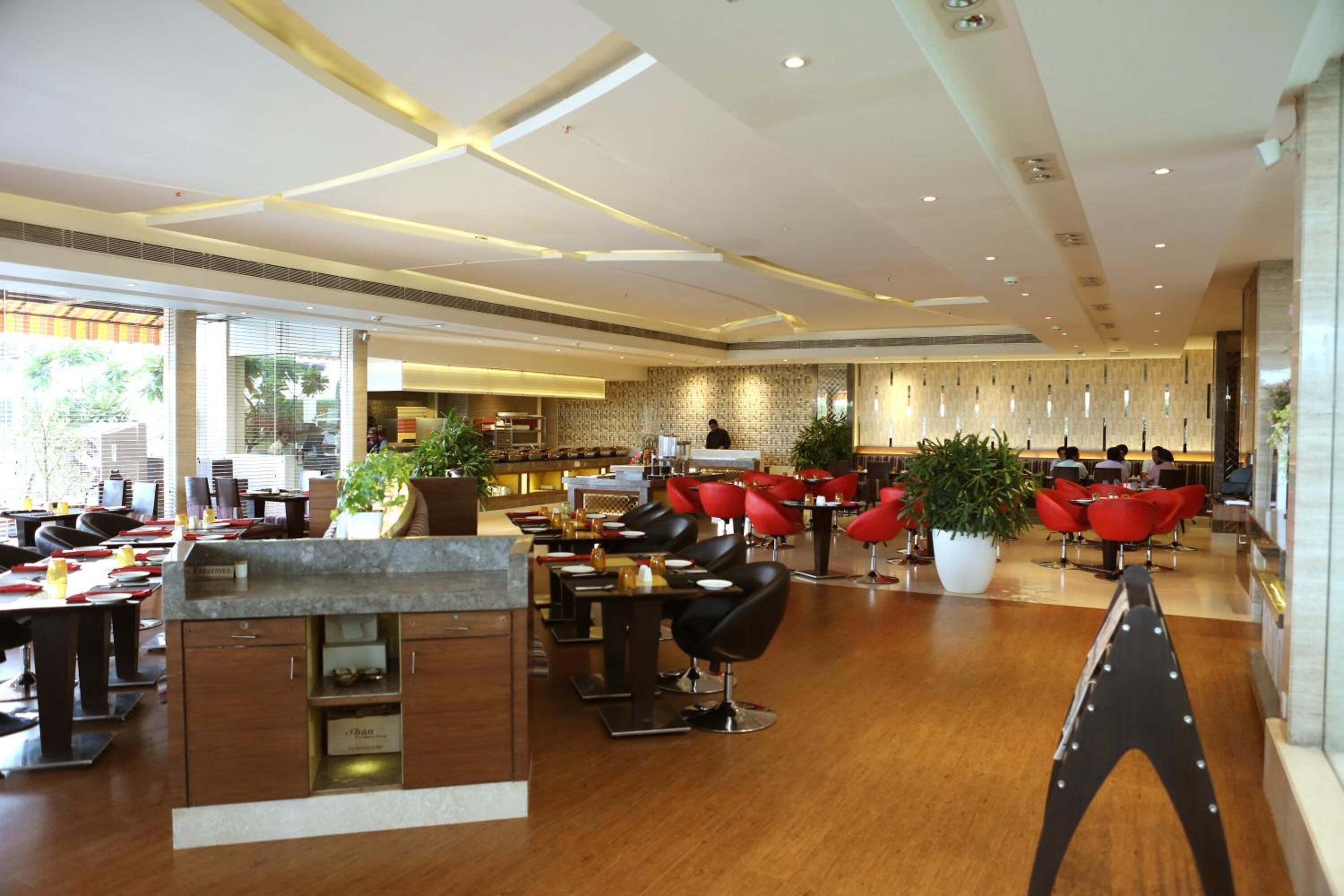 Eine moderne Hotelhalle mit einer zentralen Rezeption, mehreren Sitzbereichen mit roten Stühlen und einer Bar.