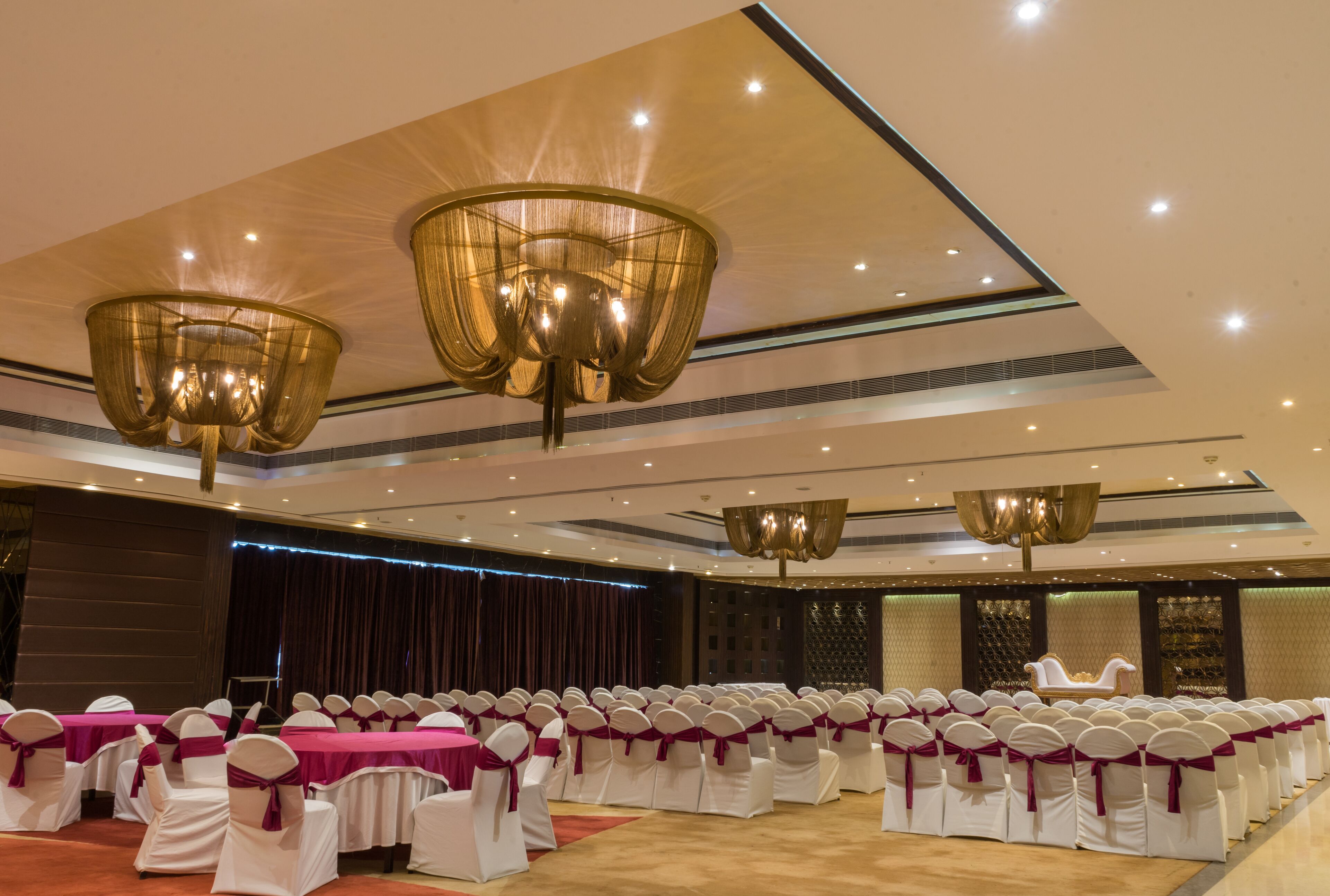 A banquet hall with rows of white chairs with purple sashes, a stage, and a large chandelier.