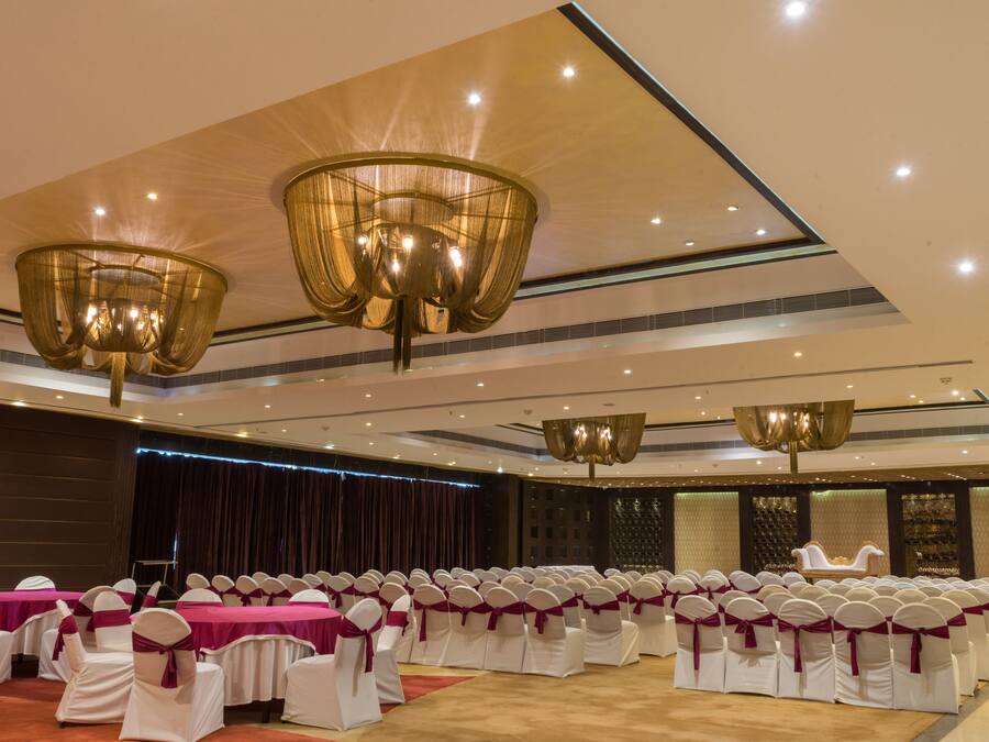 A banquet hall with rows of white chairs with purple sashes, a stage, and a large chandelier.