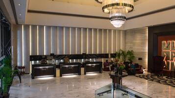 A modern hotel lobby with a reception desk, a large chandelier, and a patterned floor.