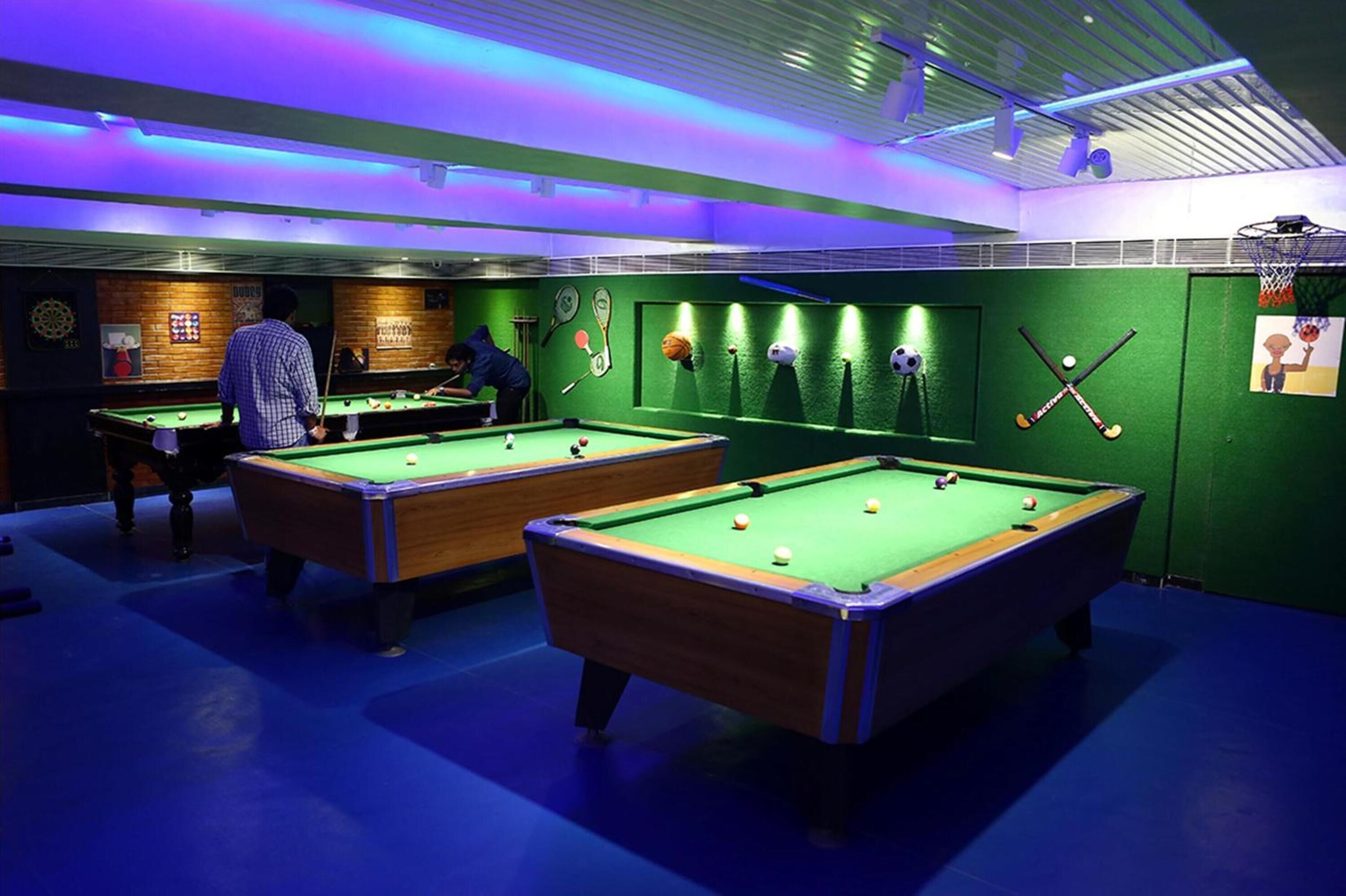Una sala de billar con dos mesas de billar, paredes verdes y equipo deportivo en las paredes.
