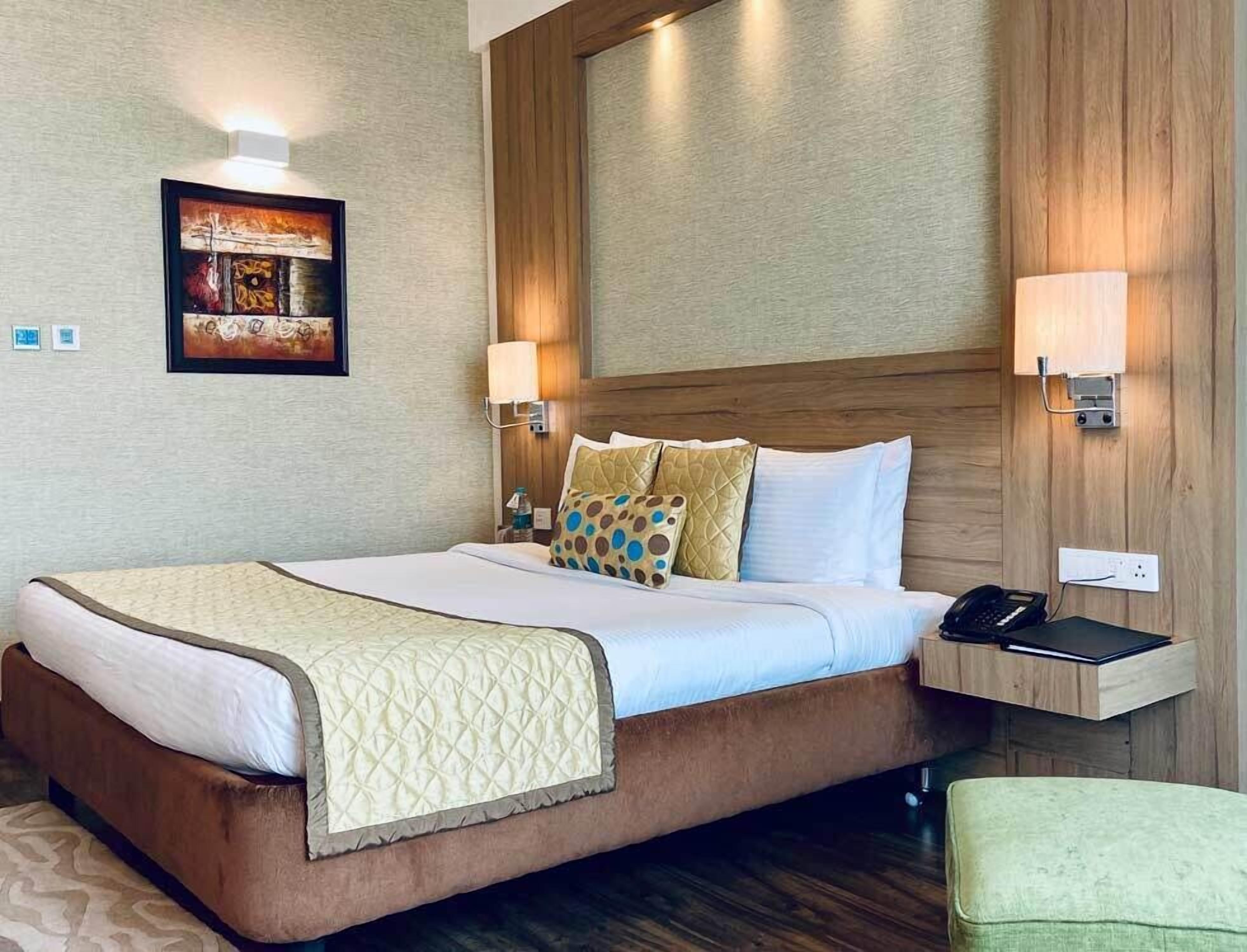 Una habitación de hotel con una cama grande, dos lámparas de noche, una mesita de noche con teléfono y un cuadro en la pared.