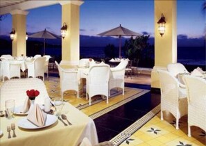 A restaurant with white tables and chairs, outdoor umbrellas, and a view of the sea. - Condo EM (Mazatlán)