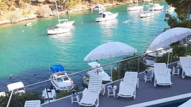 A swimming pool with lounge chairs and umbrellas, surrounded by a stone deck and overlooking a marina with boats. - Holiday apartment with terrace 200 m from the beach (Primošten)