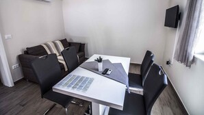 A small, modern room with a white table, black chairs, a sofa, and a TV mounted on the wall. - Holiday apartment with terrace 200 m from the beach (Primošten)