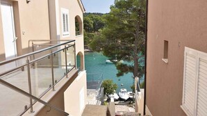 A view from a balcony overlooking a body of water with boats, trees, and a building with a beige facade. - Holiday apartment with terrace 200 m from the beach (Primošten)