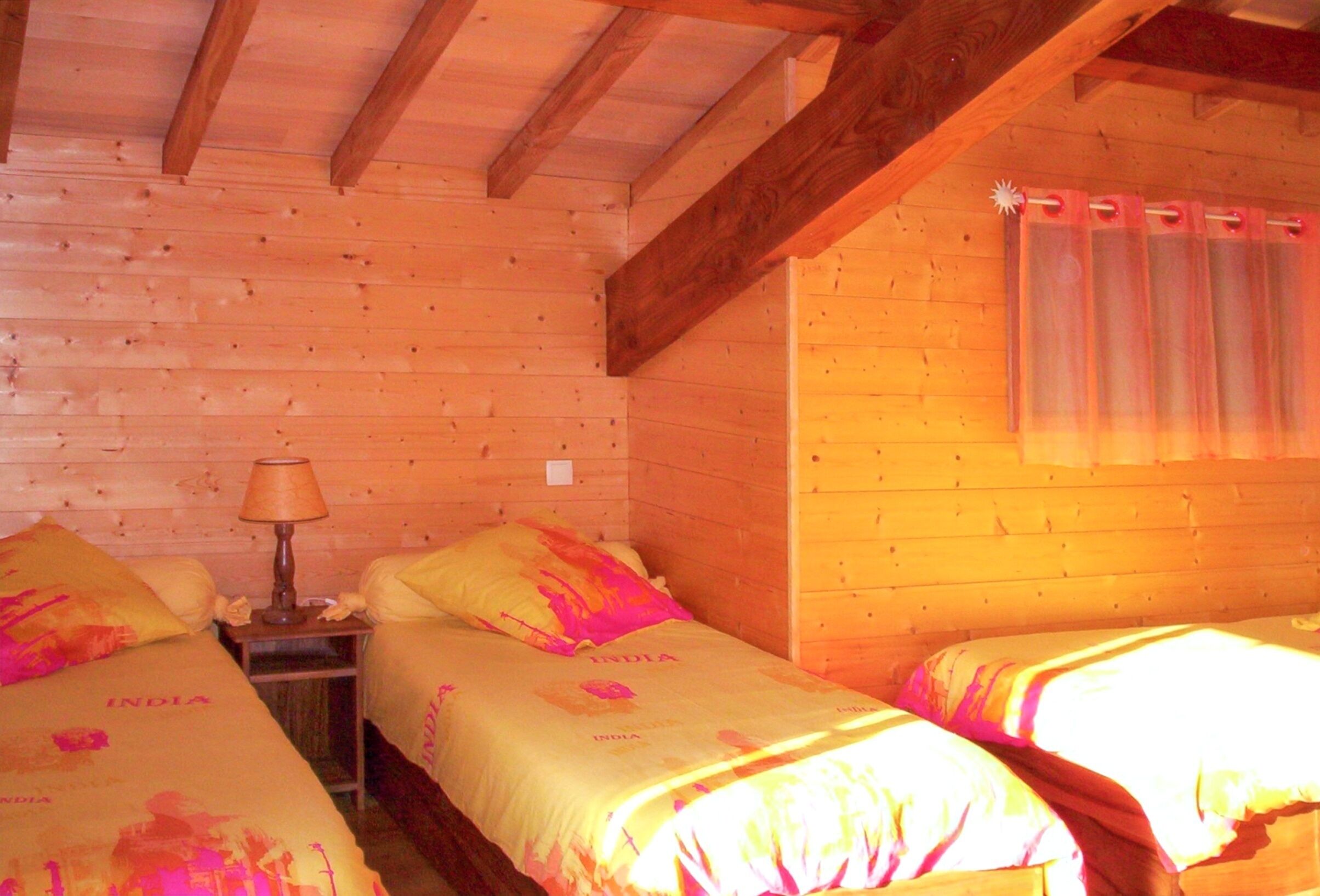 Een houten kamer met twee bedden, elk met een kussen en een lamp op een nachtkastje.