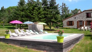 Una piscina con sillones de descanso, un edificio de piedra y una zona boscosa.