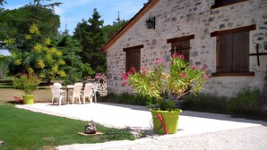 Un edificio de piedra con un patio, sillas exteriores y plantas en macetas.